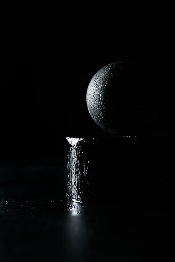 Artistic black and white image featuring a textured sphere on a pedestal with dramatic lighting.